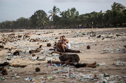 Du khách ngồi giữa bãi biển ngập rác. Ảnh: Independent.