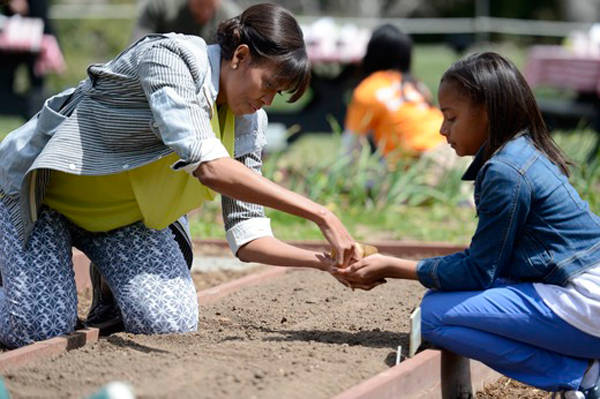 Bé Ariana Docanto, học sinh lớp 5 trường Arthur D. Healey ở thành phố Somerville, bang Massachusetts, nhận hạt giống từ tay bà Michelle khi tham gia trồng rau vào tháng 4/2013. Ảnh: AP.