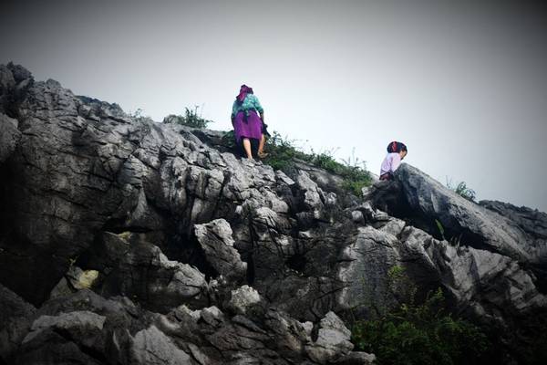 Hai cô gái vùng cao vất vả trèo lên qua những mỏm đá hái rau rừng.