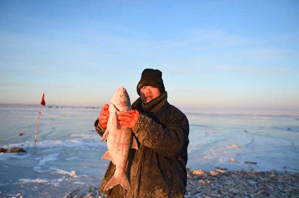 Ngư dân khoe một con cá mới câu được tại mặt hồ đóng băng Hulun (Ảnh: Xinhua)