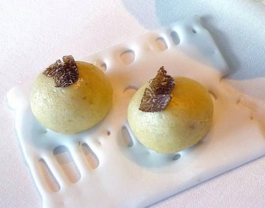 Hai miếng bánh mì nhỏ ăn kèm nấm truffle đen (một loại nấm hiếm cực ngon) được bày trên một chiếc đĩa trắng đục lỗ. Món ăn này xốp mềm và vị nấm rất đậm đà.