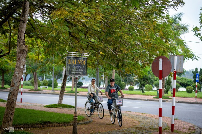 Hai du khách nước ngoài thư thả đạp xe trên đường Trần Hưng Đạo hướng về phía Đại nội Huế trong khung cảnh lá vàng mùa thu.