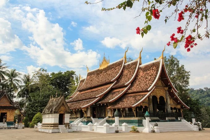 Nằm ở cuối đường Sakkarin, gần với ngã ba tiếp giáp giữa sông Mekong và sông Nam Khan, chùa Wat Xieng Thong được xây dựng năm 1560 dưới thời vua Setthathirat. Đây được xem là một trong những ngôi chùa cổ nhất của cố đô Luang Prabang, Lào. Chùa Wat Xieng Thong có chánh điện mang phong cách kiến trúc đặc trưng của Luang Prabang cổ với mái lợp ba tầng hạ sâu hướng về mặt đất, bao quanh là những miếu đường nhỏ có cùng một lối kiến trúc. Ngoài ra, chùa còn nổi bật với những bức tranh đa sắc màu về lịch sử Phật giáo và lịch sử dân tộc, được các họa sĩ dùng miếng sành, sứ lắp ghép tỉ mỉ lại với nhau hoặc trực tiếp vẽ lên tường, tạo nên các tác phẩm nghệ thuật độc đáo. Ảnh: Maria Globetrotter.