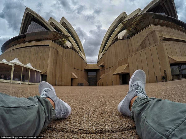 Nhiếp ảnh gia người Úc ngồi bệt sau nhà hát Opera Sydney nổi tiếng của Úc.