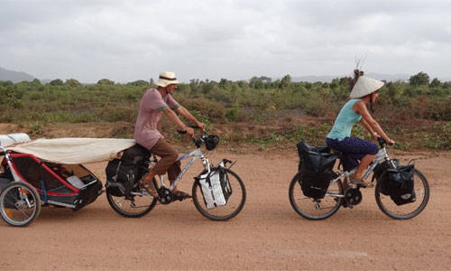 Hai vợ chồng đạp xe cùng hai con đi dọc sông Mê Kông.